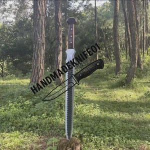 May include: A large sword with a brown handle and a silver blade is displayed outdoors. A smaller knife with a black handle is drawn over the sword. The text "HANDMADEKNIFE01" is printed on the image.