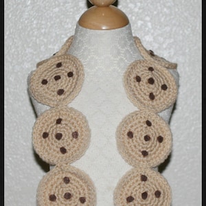 May include: A crocheted necklace designed to resemble chocolate chip cookies. The necklace is made from brown and beige yarn and features a brown yarn design to look like chocolate chips.
