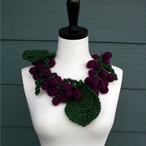 May include: A purple and green crocheted grapevine necklace with leaves and grapes.