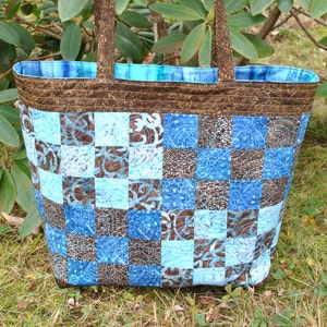 Peut inclure: Un sac fourre-tout en patchwork marron et bleu avec des anses marrons. Le sac est fait de carrés de tissu à motif floral.