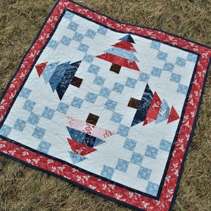 Puede incluir: Una colcha blanca con un patrón a cuadros y cuatro árboles de patchwork azul, rojo y blanco. La colcha tiene un borde rojo, blanco y azul con un patrón floral.