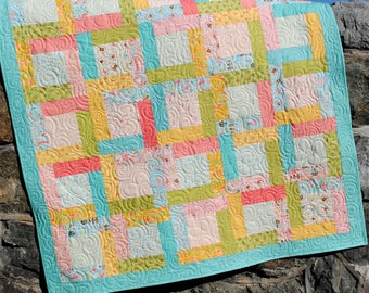 Puede incluir: Una colcha de retazos colorida con un borde turquesa. La colcha está hecha de cuadrados de diferentes telas en tonos de rosa, amarillo, verde y azul. La colcha está acolchada con un patrón de espiral.