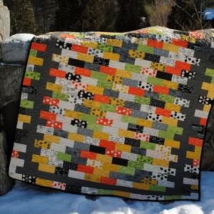 May include: A colorful patchwork quilt with a geometric pattern of squares and rectangles in shades of gray, orange, yellow, green, and white. The quilt is made of different fabrics with various patterns and textures.