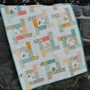 Op de afbeelding: Een wit quilt met een patchwork-ontwerp met verschillende bosdieren en bloemenpatronen. Het quilt is gemaakt van verschillende stoffen in tinten roze, groen, geel en bruin. Het quilt is gequilt met een draaiend patroon.