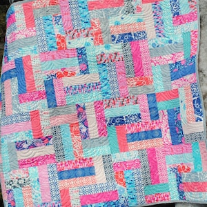 May include: A patchwork quilt with a variety of colorful fabrics in shades of pink, blue, and gray. The quilt is made up of rectangular pieces of fabric sewn together in a staggered pattern.