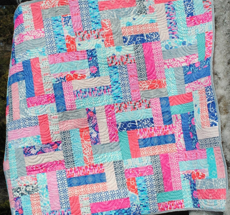 May include: A patchwork quilt with a variety of colorful fabrics in shades of pink, blue, and gray. The quilt is made up of rectangular pieces of fabric sewn together in a staggered pattern.