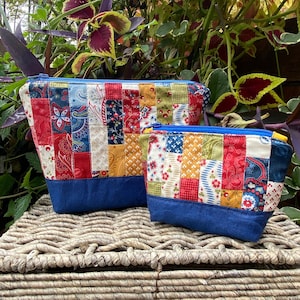 Puede incluir: Dos bolsas con cremallera de tela de patchwork, una más grande que la otra. Las bolsas están hechas de una variedad de telas coloridas, incluyendo rojo, azul, amarillo y verde. Las bolsas tienen un ribete de mezclilla azul.