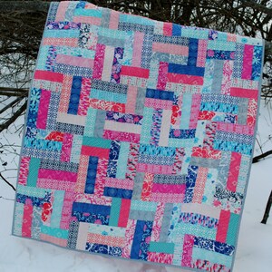 May include: A patchwork quilt with a geometric pattern in shades of pink, blue, and white. The quilt is made of various fabrics with different patterns and textures.