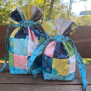 Peut inclure: Deux sacs à cordon en patchwork bleu et vert avec des accents dorés. Les sacs sont faits de chutes de tissu et ont un aspect matelassé.