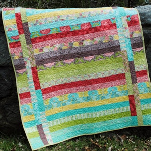 May include: A colourful quilt with a patchwork design featuring stripes of various colours, including red, pink, yellow, green, and blue. The quilt is made with different patterned fabrics and is quilted with a wavy design.