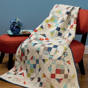 May include: A colorful patchwork quilt draped over a red chair. The quilt features squares and triangles in various patterns and colors, including blue, red, green, and gray, with a cream-colored background. The quilt has a dark blue border.