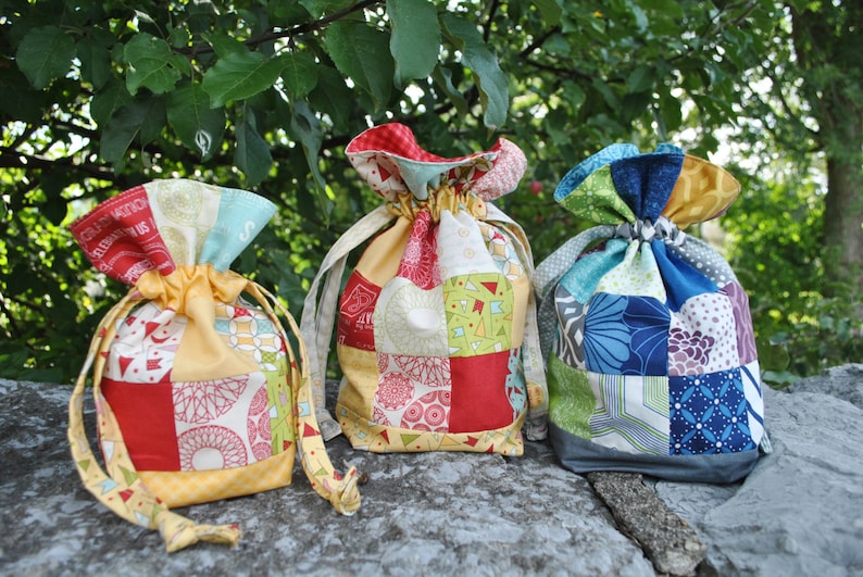 Peut inclure: Trois sacs &agrave; cordon de couleur faits de tissu patchwork. Les sacs sont rouge, jaune, bleu, vert et blanc. Les sacs sont pos&eacute;s sur une surface de pierre grise.