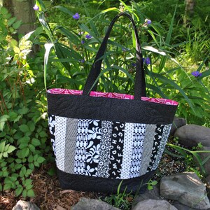 May include: A black and white patchwork tote bag with a pink lining. The bag has a black fabric handle and is made of different patterned fabrics.