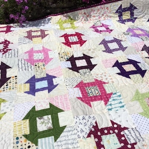 May include: A patchwork quilt with a white background and colourful squares. The squares are arranged in a pattern of interlocking squares, with each square featuring a different fabric. The quilt is quilted with a simple stitch pattern.