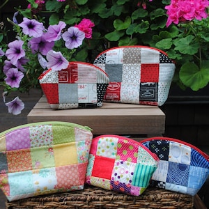 May include: Five patchwork fabric zippered pouches in various colors and patterns. The pouches are arranged on a wooden surface with a wicker basket in front of them.