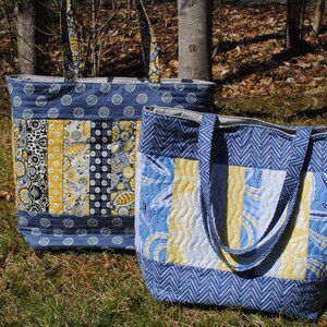 May include: Two quilted tote bags with blue and yellow fabric. The larger bag has a chevron pattern and the smaller bag has a patchwork design.
