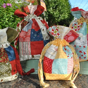 Peut inclure: Quatre sacs &agrave; cordon en tissu patchwork color&eacute;s avec diff&eacute;rents motifs et designs. Les sacs sont en tissu de coton et ont une palette de couleurs rouge, blanche et bleue. Les sacs sont parfaits pour ranger de petits objets ou des cadeaux.