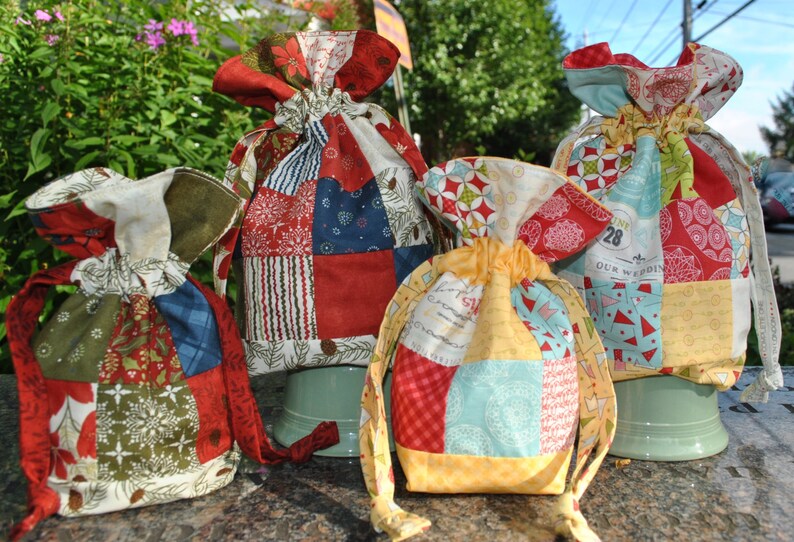 Peut inclure: Quatre sacs &agrave; cordon en tissu patchwork color&eacute;s avec diff&eacute;rents motifs et designs. Les sacs sont en tissu de coton et ont une palette de couleurs rouge, blanche et bleue. Les sacs sont parfaits pour ranger de petits objets ou des cadeaux.