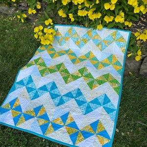 May include: A blue, yellow, and green patchwork quilt with a white background. The quilt is made of various fabrics with different patterns and is quilted with a swirling design.