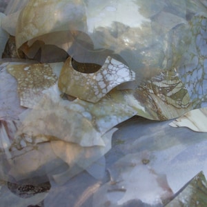 May include: Abstract composition of overlapping, translucent, irregularly shaped pieces. The pieces display a variety of patterns, including marbled and speckled designs in shades of beige, cream, and pale blue. The overall effect is layered and textured.