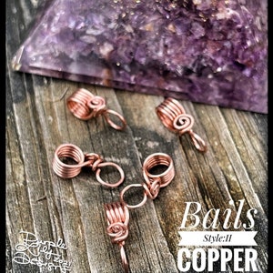 May include: Copper bails, Style II, are displayed on a weathered wooden surface. The handmade jewelry findings are in a spiral and coil design. The image also includes a purple crystal and the text "Bails, Style: II, COPPER".