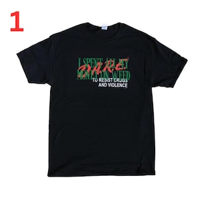 May include: Black t-shirt with the text "I SPENT ALL MY MONEY ON WEED TO RESIST DRUGS AND VIOLENCE" in green and red. The number "1" is in red in the upper left corner.