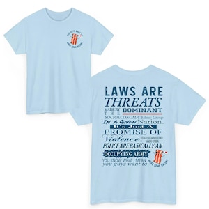 May include: Light blue t-shirts with graphic text and illustrations. One shirt features a bacon illustration and the text "YOU GUYS WANT TO MAKE SOME BACON?". The other shirt has text that reads "LAWS ARE THREATS" and a bacon illustration.