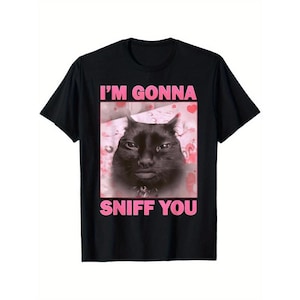 May include: Black t-shirt featuring a close-up of a black cat with the text "I'M GONNA SNIFF YOU" in pink. The cat has a slightly grumpy expression. The background is a pink and white pattern with hearts.