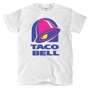 May include: White t-shirt featuring the Taco Bell logo. The logo includes a pink bell with a yellow accent inside a blue arch, and the words "TACO BELL" in blue below.