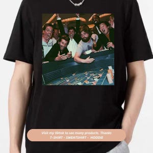 May include: A group of people are gathered around a green felt casino table with chips and dice. The people are all smiling and laughing, and one person is holding up a handful of chips. The image is a black and white photograph.