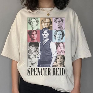 May include: A beige t-shirt with a collage of images of a man with different hairstyles and facial expressions. The text "Spencer Reid" is printed in black at the bottom of the shirt.