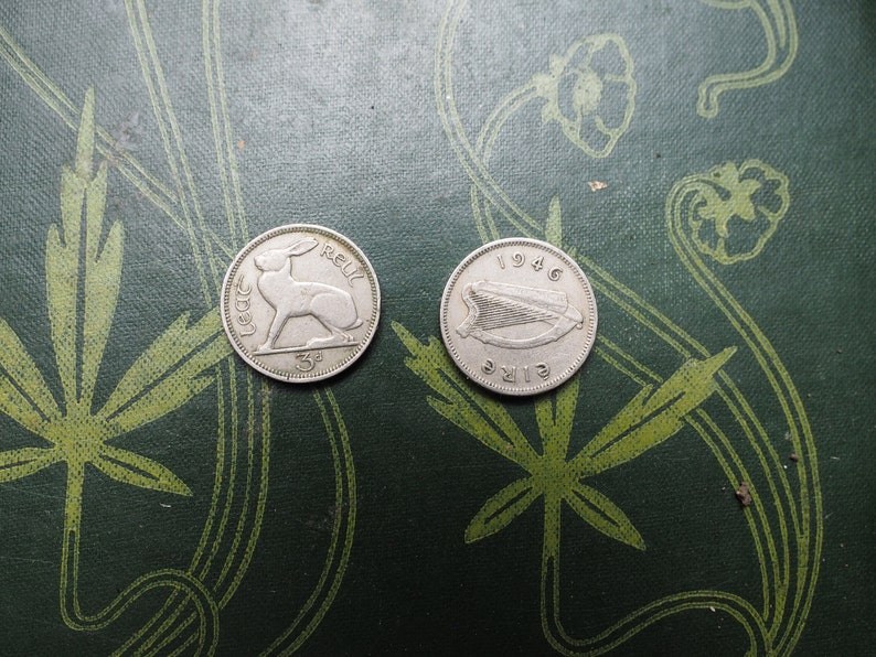 May include: Two silver Irish coins on a green background. The first coin features a hare and the text "IRELAND" and "3d". The second coin features a harp and the text "EIRE" and "1946".
