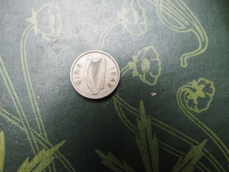 May include: A silver Irish coin with the year 1942 and the word "EIRE" inscribed around the edge. The coin features a harp in the center.