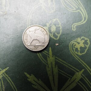 May include: A silver Irish coin with a hare or rabbit design and the text "3d" and "Eire" on it.