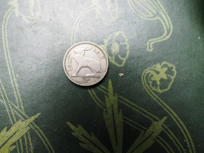 May include: A silver Irish coin with a hare or rabbit design and the text "3d" and "Eire" on it.