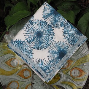 May include: A white fabric napkin with a blue and white floral pattern. The napkin has a white lace trim around the edges.