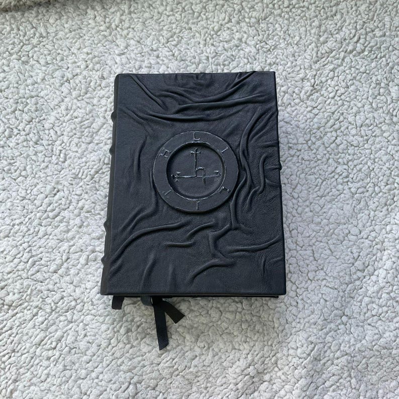May include: A black, embossed book with a circular emblem on the cover. The emblem features a cross-like symbol within a ring. The book has a textured, wrinkled appearance and a black ribbon bookmark.