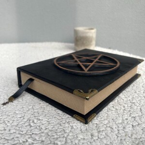 May include: Black leather-bound journal with a pentagram design on the cover. The journal has a brown ribbon bookmark and gold-toned corner accents.