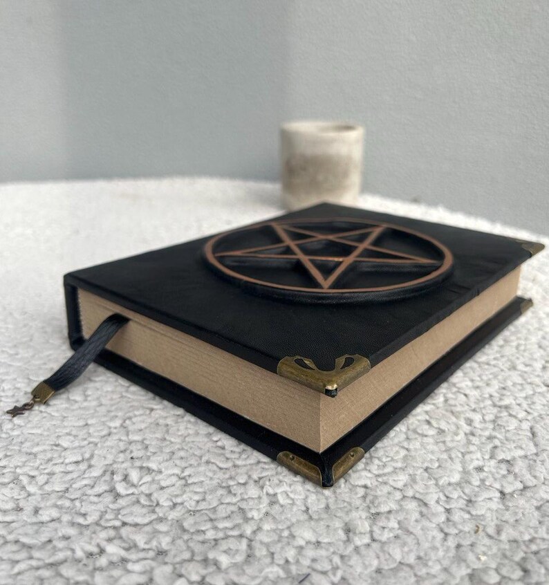 May include: Black leather-bound journal with a pentagram design on the cover. The journal has a brown ribbon bookmark and gold-toned corner accents.