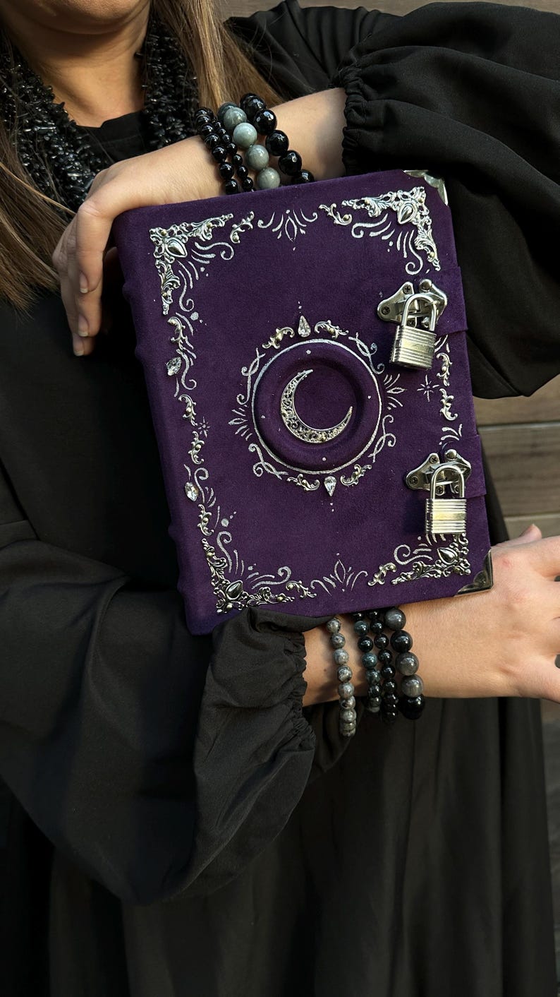 May include: A purple journal with silver detailing and a crescent moon motif. The journal features a lock closure and decorative corners. The cover is a deep purple, with silver accents providing contrast. A unique and stylish item, the journal is a great gift.
