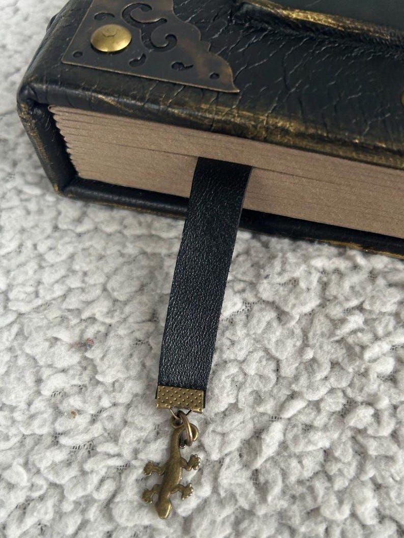 Pode incluir: Um di&aacute;rio encadernado em couro preto com um fecho de lat&atilde;o e um marcador de couro preto com um amuleto de lagarto dourado.