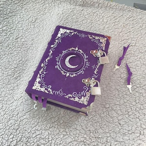 May include: A purple journal featuring a crescent moon design and silver embellishments. The journal is secured with a lock and key, with two keys and a ribbon bookmark. The cover is decorated with ornate silver filigree.