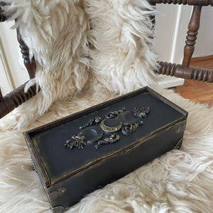 May include: A set of three ceramic mugs with a speckled, cream-colored glaze. Each mug features a different hand-painted design: a blue and green leaf, a yellow flower, and a red berry. The mugs have a simple, rounded shape.