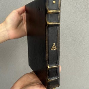Pode incluir: Di&aacute;rio encadernado em couro preto com detalhes dourados e um fecho de metal decorativo. O di&aacute;rio tem um design de n&oacute; celta na lombada.