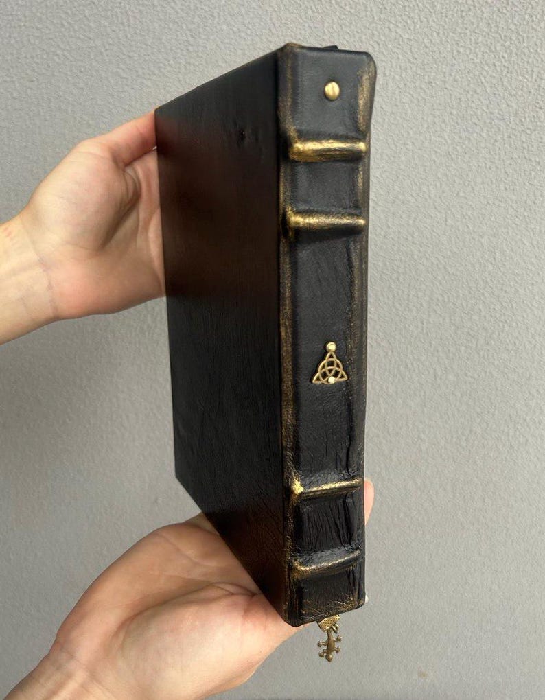 Pode incluir: Di&aacute;rio encadernado em couro preto com detalhes dourados e um fecho de metal decorativo. O di&aacute;rio tem um design de n&oacute; celta na lombada.