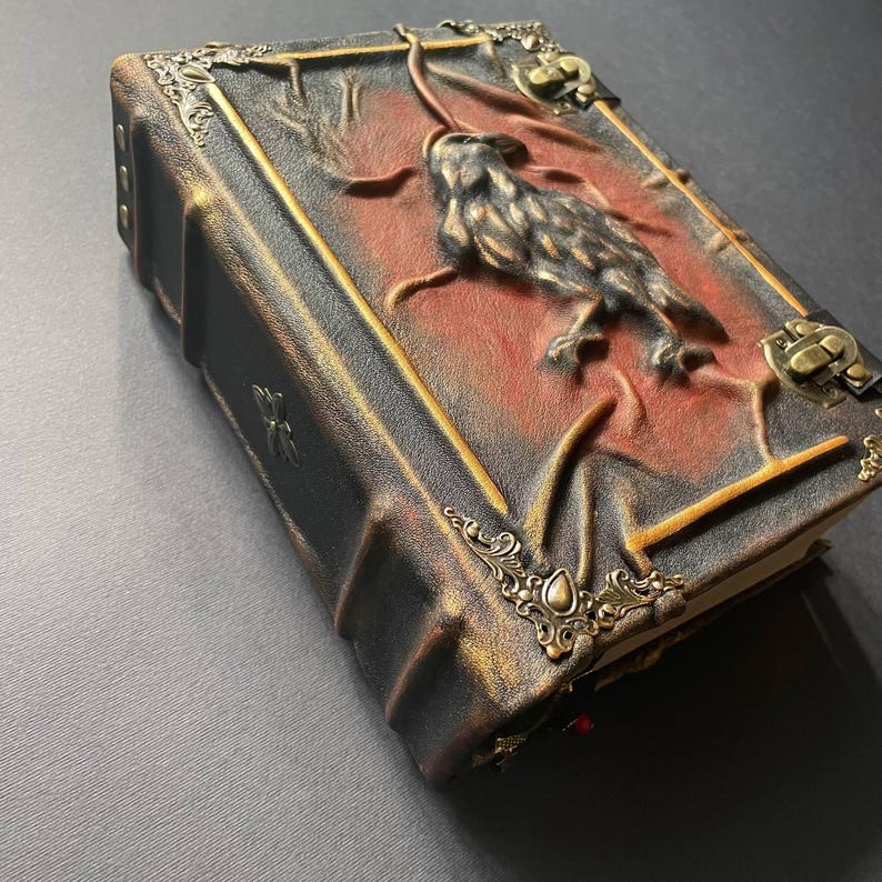 K&ouml;nnte beinhalten: Ein handgefertigtes, ledergebundenes Buch mit einem gepr&auml;gten Eulenmotiv. Der Einband hat eine dunkelbraune und rote Farbgebung mit goldenen Akzenten und verzierten Metallecken. Das Buch hat eine Vintage- und Gothic-&Auml;sthetik.