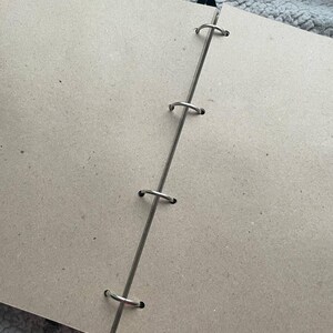 May include: Open view of a blank, light brown scrapbook with a silver metal binding. The binding has four metal rings. The pages are a neutral, solid color, and the book is open, ready for use.