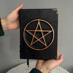 May include: Black leather journal with a gold pentagram design on the front cover.