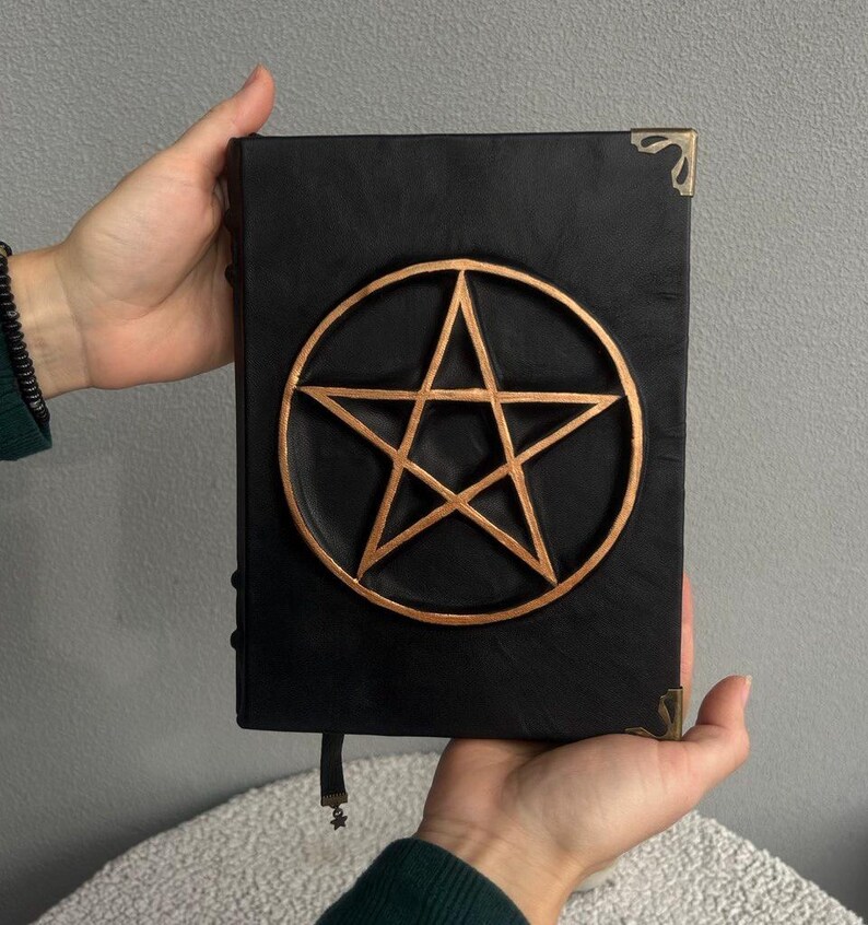 May include: Black leather journal with a gold pentagram design on the front cover.