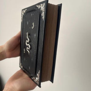 Op de afbeelding: Een zwart lederen gebonden dagboek met zilveren accenten en een slangontwerp. De omslag heeft een halve maan en sterren.